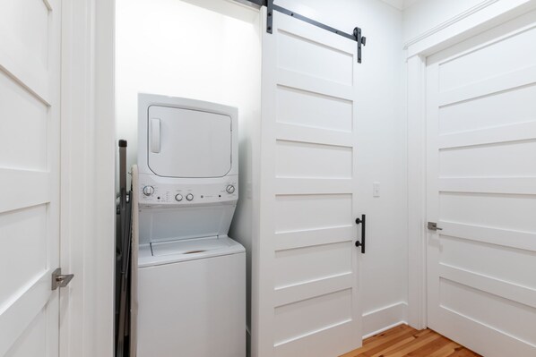 A laundry room with a front-loading washer and dryer, a metal rack, and white doors.