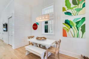 A dining area with a white table and bench, a basket on the table, and a wall with abstract art.