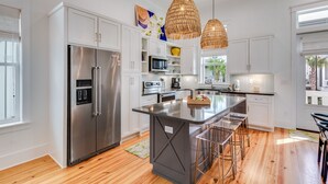 A modern kitchen with a central island, stainless steel appliances, white cabinetry, and a large window providing natural light.