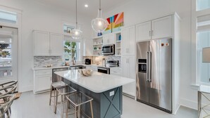 A modern kitchen with white cabinetry, stainless steel appliances, and a central island with stools.