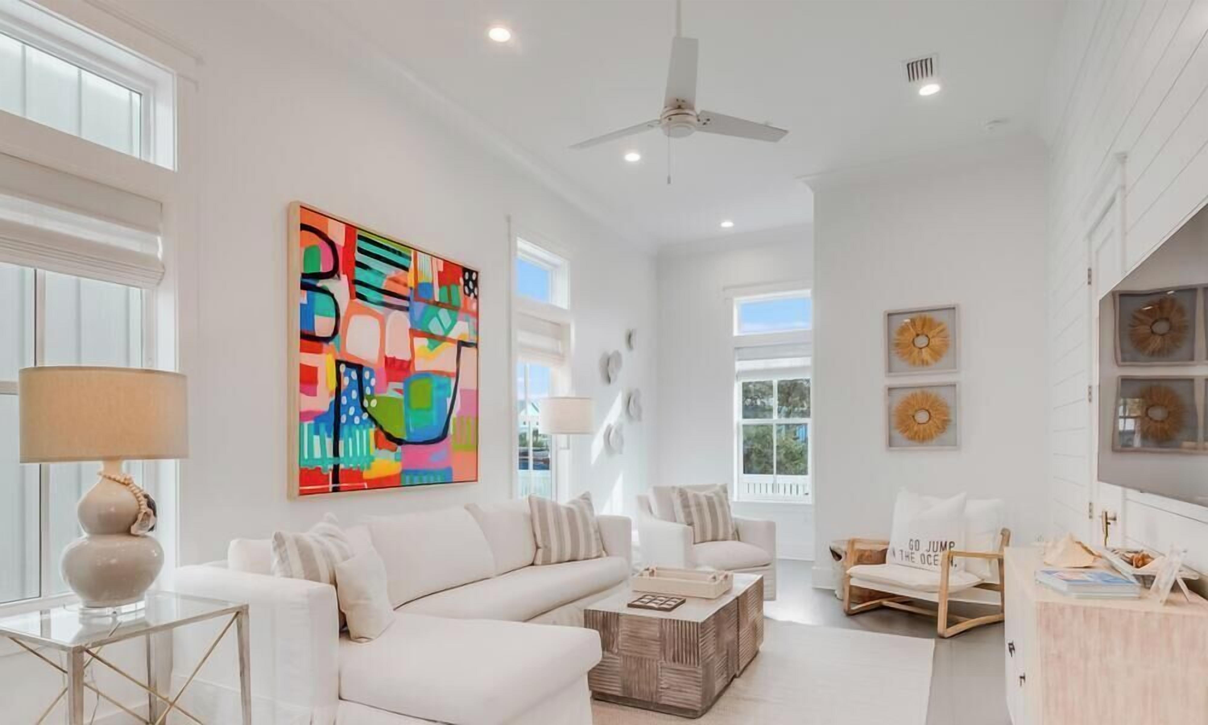 A spacious living room with a white sofa, a coffee table, and a colorful abstract painting.