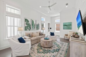 A spacious living room with a large window, a ceiling fan, and a flat-screen TV mounted on the wall. - BVR 67 - Kit Kamp by Liquid Life (Orange Beach)