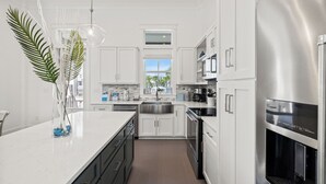 A modern kitchen with white cabinetry, stainless steel appliances, and a large island with a glass vase. - BVR 67 - Kit Kamp by Liquid Life (Orange Beach)