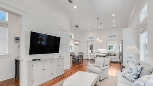 A spacious living room with a large flat-screen TV, white cabinetry, and a dining area with a table and chairs.