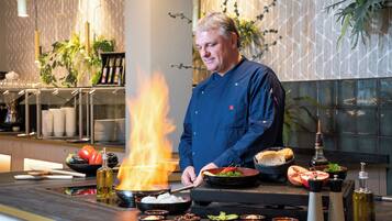 A chef cooking at a professional kitchen with a fire, various cooking utensils, and ingredients.