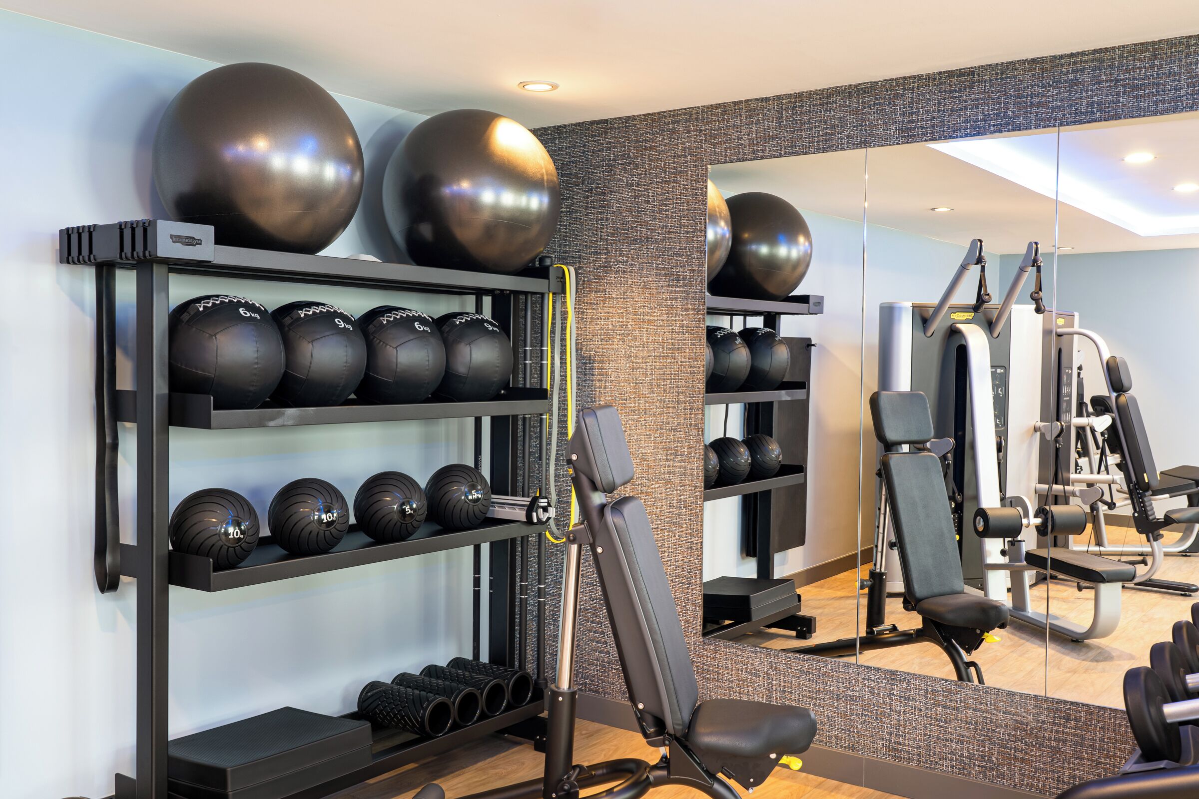 Uma academia com equipamentos de ginástica, incluindo um banco, um espelho e várias bolas de fitness.