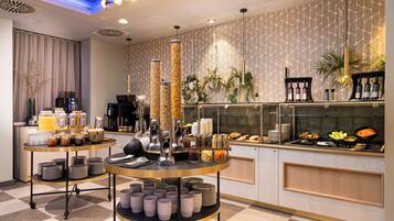 A modern breakfast bar with a variety of food items, a coffee station, and decorative plants.