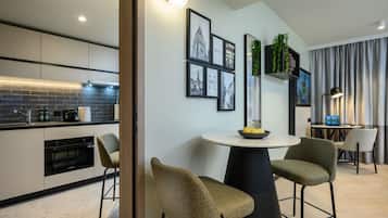 A modern kitchen with a built-in oven, a dining area with a round table and two chairs, and a wall with framed pictures and a plant.