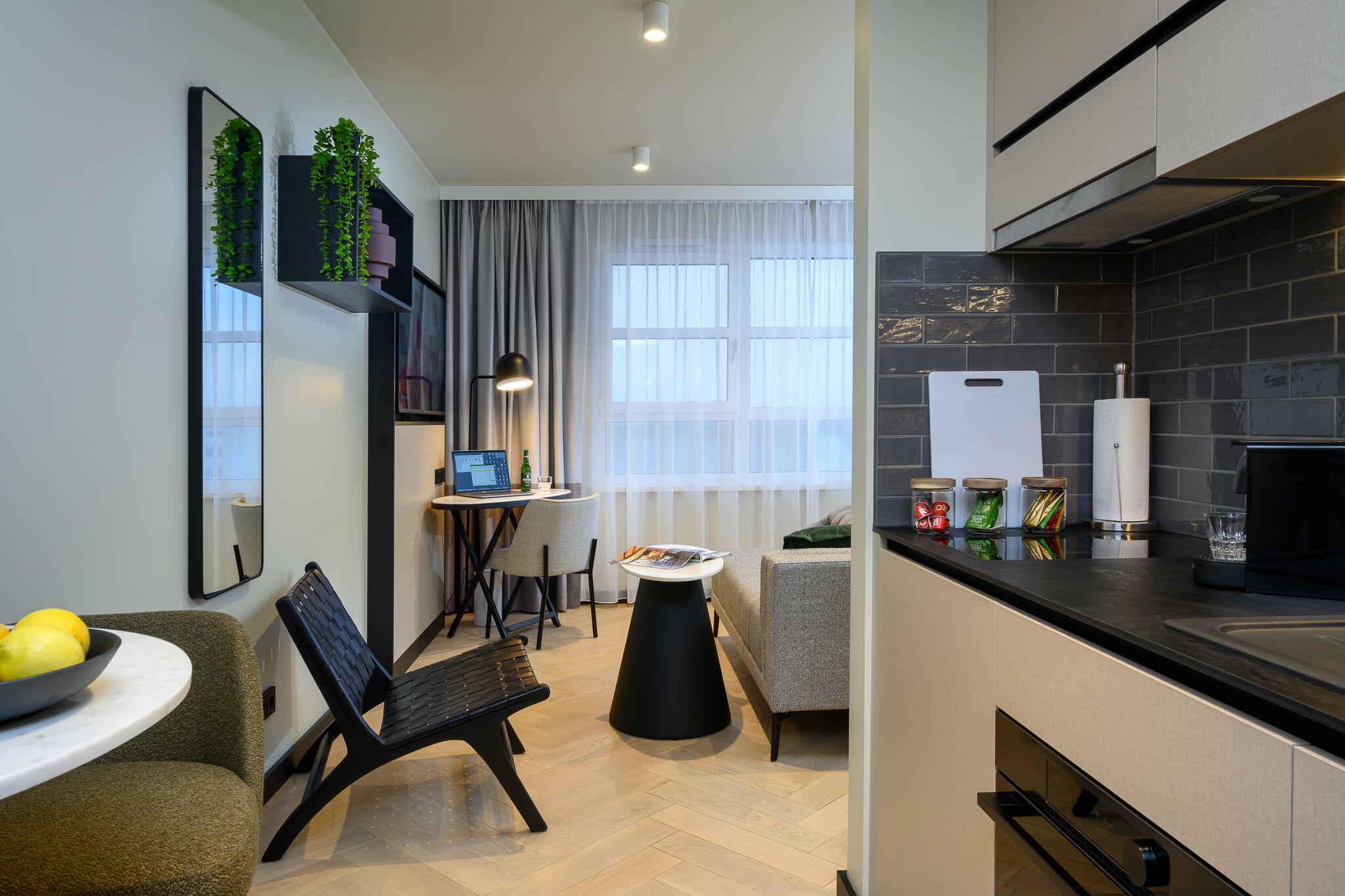 Una cocina moderna con encimera negra, un comedor con mesa y sillas redondas, y una pequeña zona de estar con un banco.