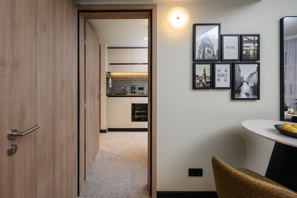 Una cocina moderna con puerta de madera, zona de comedor con mesa redonda y cuadros con vistas de la ciudad en la pared.