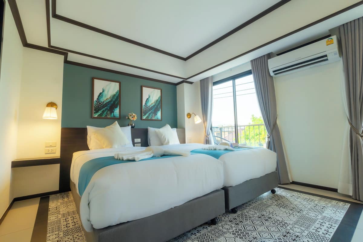 A double bed with a grey headboard, two wall-mounted lamps, and a window with curtains.
