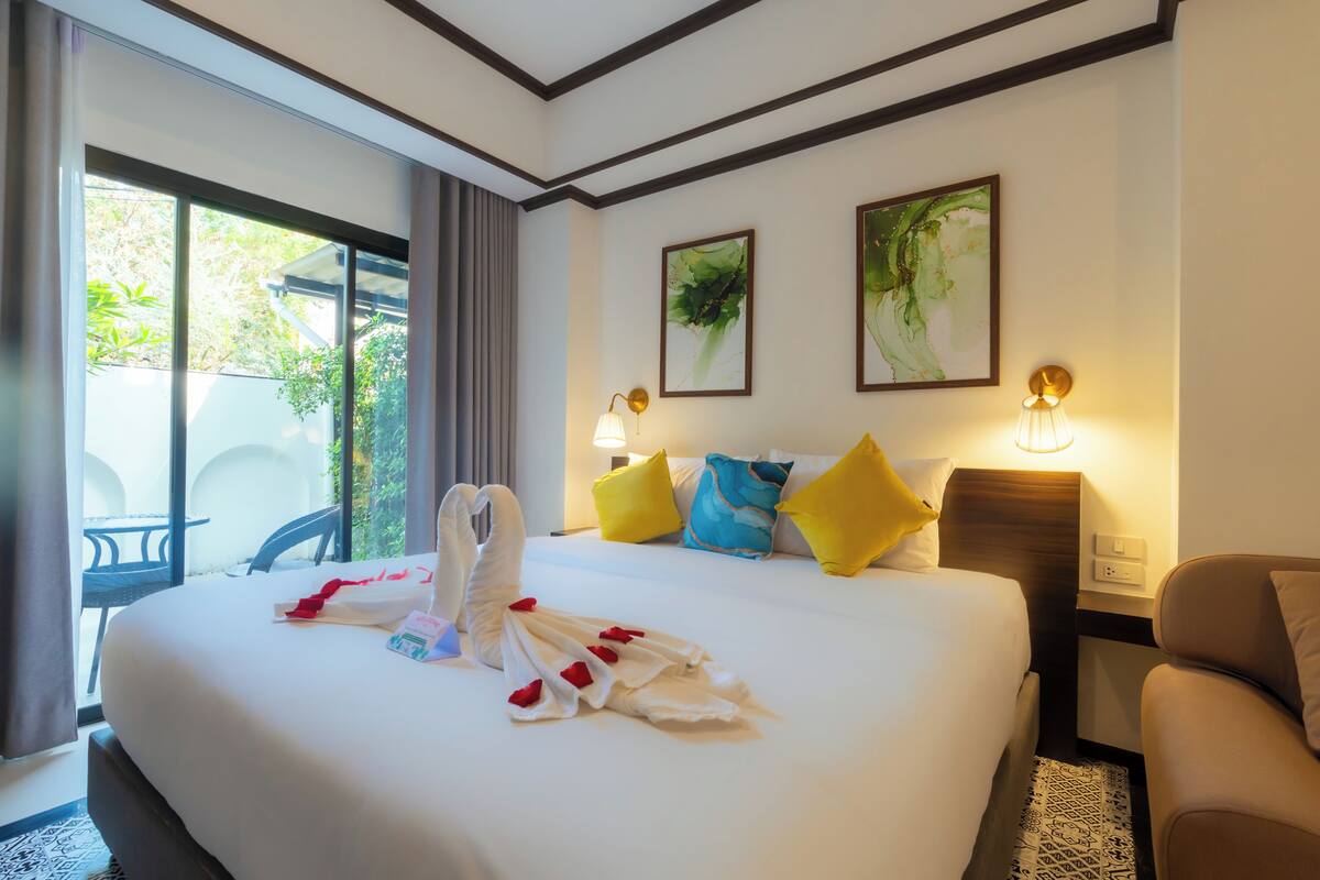 A hotel room with a large bed, two bedside lamps, a headboard, and a view of the outdoors.