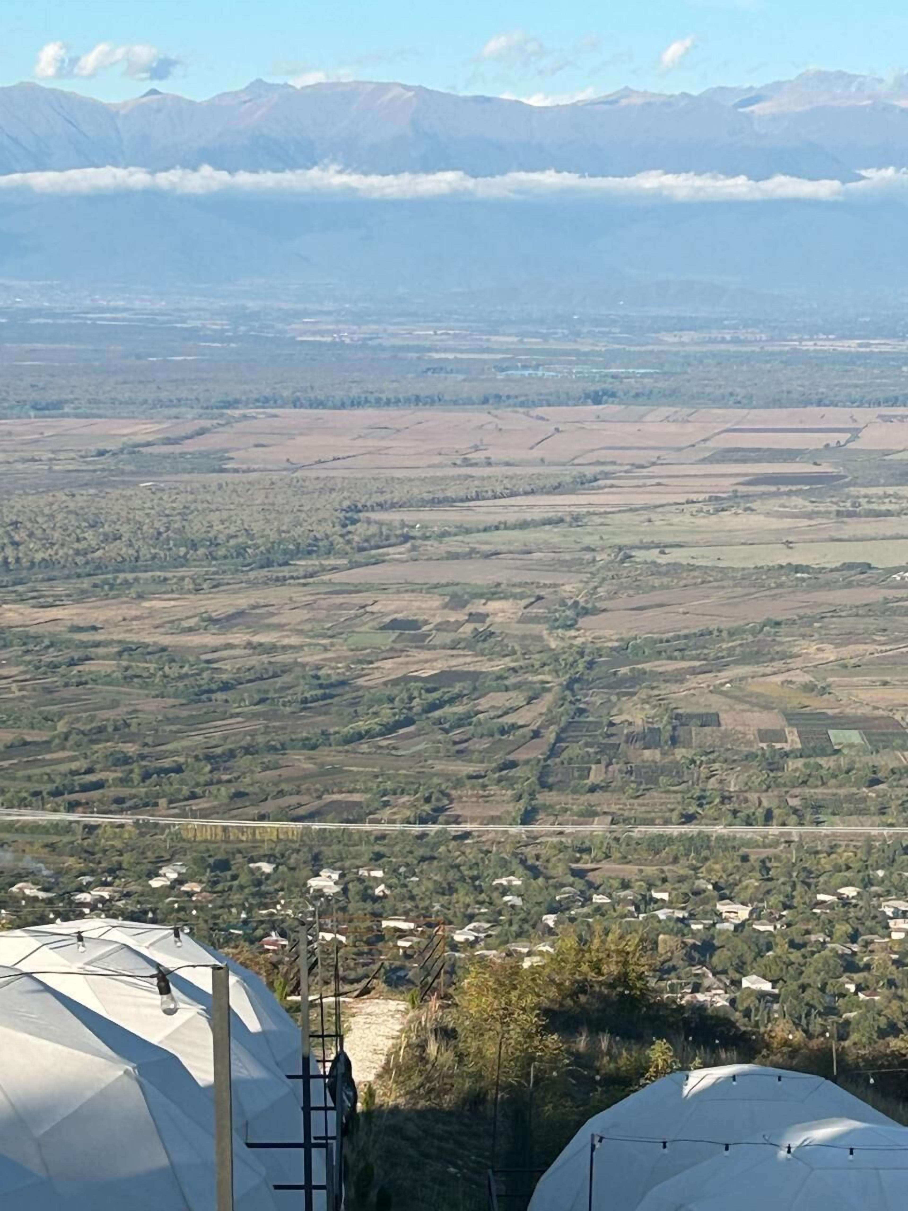 Paisaje rural con campos, un pequeño pueblo y montañas al fondo.
