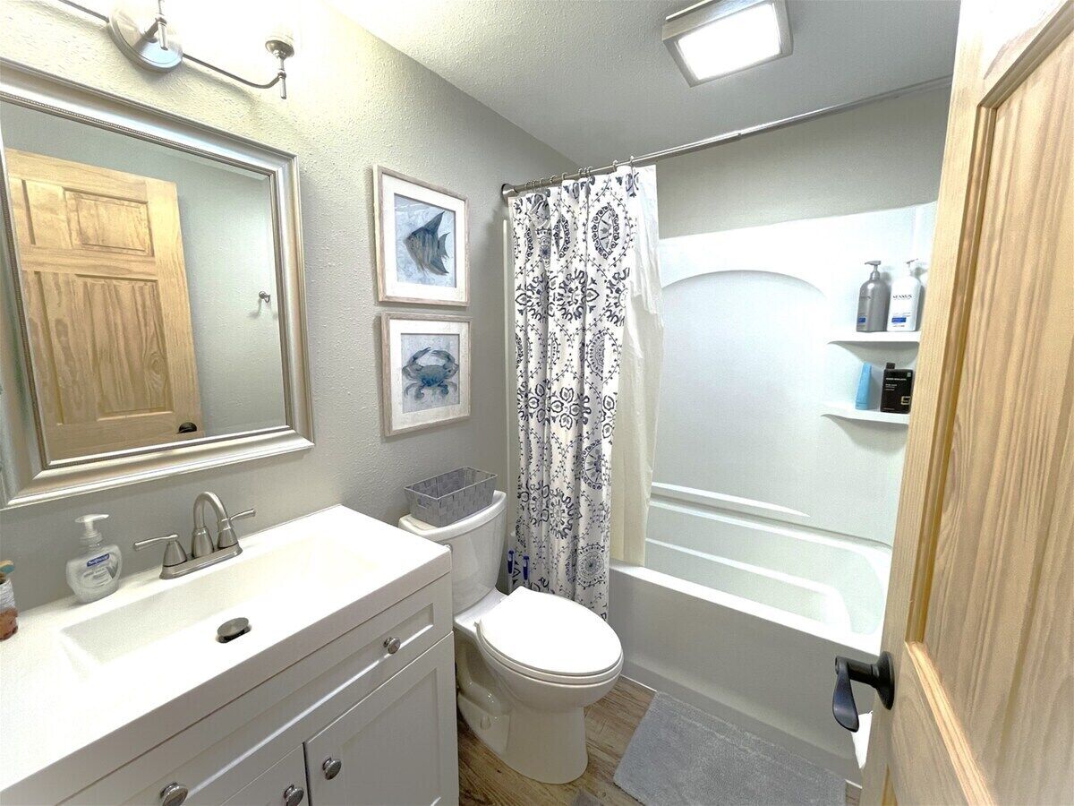A bathroom with a white sink, a toilet, a shower with a patterned curtain, and a wooden door.
