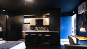 A compact hotel room with a kitchenette, a bed, a small dining area, and a blue accent wall. - Montrose Ash Studio! Medical Center 03 (Houston)