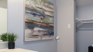 A bathroom with a white sink, a potted plant, and a large abstract painting on the wall.