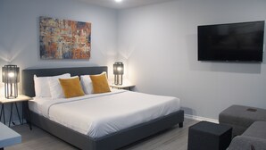 A modern bedroom with a large bed, two bedside tables with lamps, a flat-screen TV, and a gray sofa.
