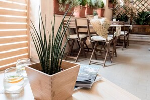A wooden planter with a tall plant, a table with glasses of water, and a magazine on a wooden table in a cozy outdoor setting. - Resilience Tropical Apartments&Room (App. Pineapple) (Porto Sant'Elpidio)