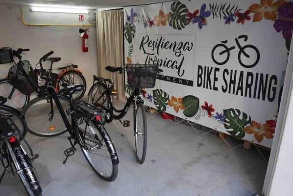 A bike-sharing station with a tropical-themed sign, multiple bicycles, and a fire extinguisher on the wall.