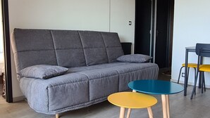 A living room with a grey sofa, a blue and yellow table, and a decorative ceiling light. - F2 Confortable, à 2 Minutes de la Plage et du Port (CARNON-PLAGE)
