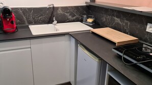 A kitchen with a white sink, a red coffee maker, a wooden cutting board, and a stove. - F2 Confortable, à 2 Minutes de la Plage et du Port (CARNON-PLAGE)