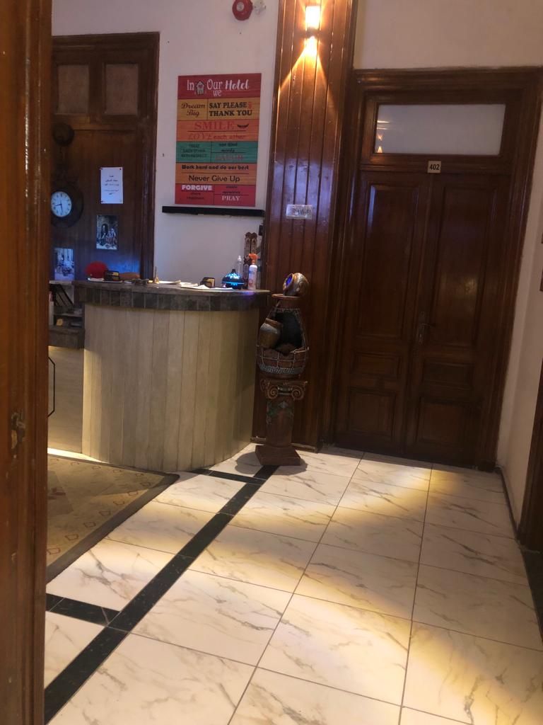 Un espace d’accueil d’hôtel avec un comptoir de réception en bois, une horloge et un panneau affichant un message.