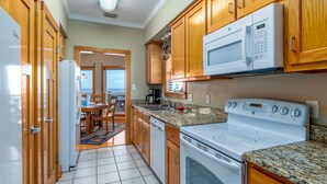 A modern kitchen with wooden cabinets, a microwave, a stove, and a dining area with a view. - New to Vrbo! "Dues Paid" Waterfront, Boat Dock, 3 Bedrm/2.5 Bath, Sleeps 6 (Dauphin Island)
