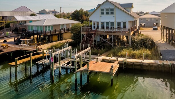 A waterfront property with a main house, dock, and adjacent smaller buildings. - New to Vrbo! "Dues Paid" Waterfront, Boat Dock, 3 Bedrm/2.5 Bath, Sleeps 6 (Dauphin Island)