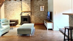 A rustic living room with exposed wooden beams, a brick wall, a fireplace, a sofa, a TV, and a small table. - Cosy holiday home in Flanders Fields and at 10min from the sea. Pets welcome! (Alveringem)
