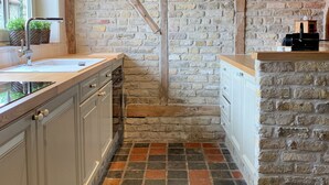 A kitchen with a brick wall, wooden beams, and a tiled floor. - Cosy holiday home in Flanders Fields and at 10min from the sea. Pets welcome! (Alveringem)