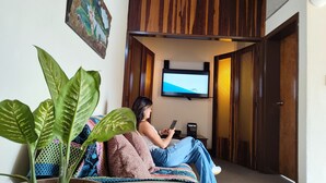 A person sitting on a couch in a room with a television mounted on the wall, a potted plant, and a wooden door. - Casa Cumbre: Un hospedaje único en Mérida, con la mejor vista a la Sierra Nevada (Merida)