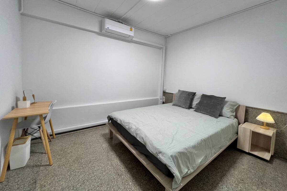 A bedroom with a bed, bedside table, lamp, and a desk with chair.