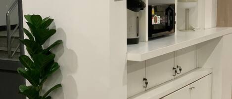 A white kitchen with a microwave, a coffee maker, and a plant.