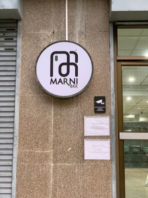 A building with a circular sign that reads "MARNI BKK" on a textured wall. - Marni BKK Hostel (Bangkok)