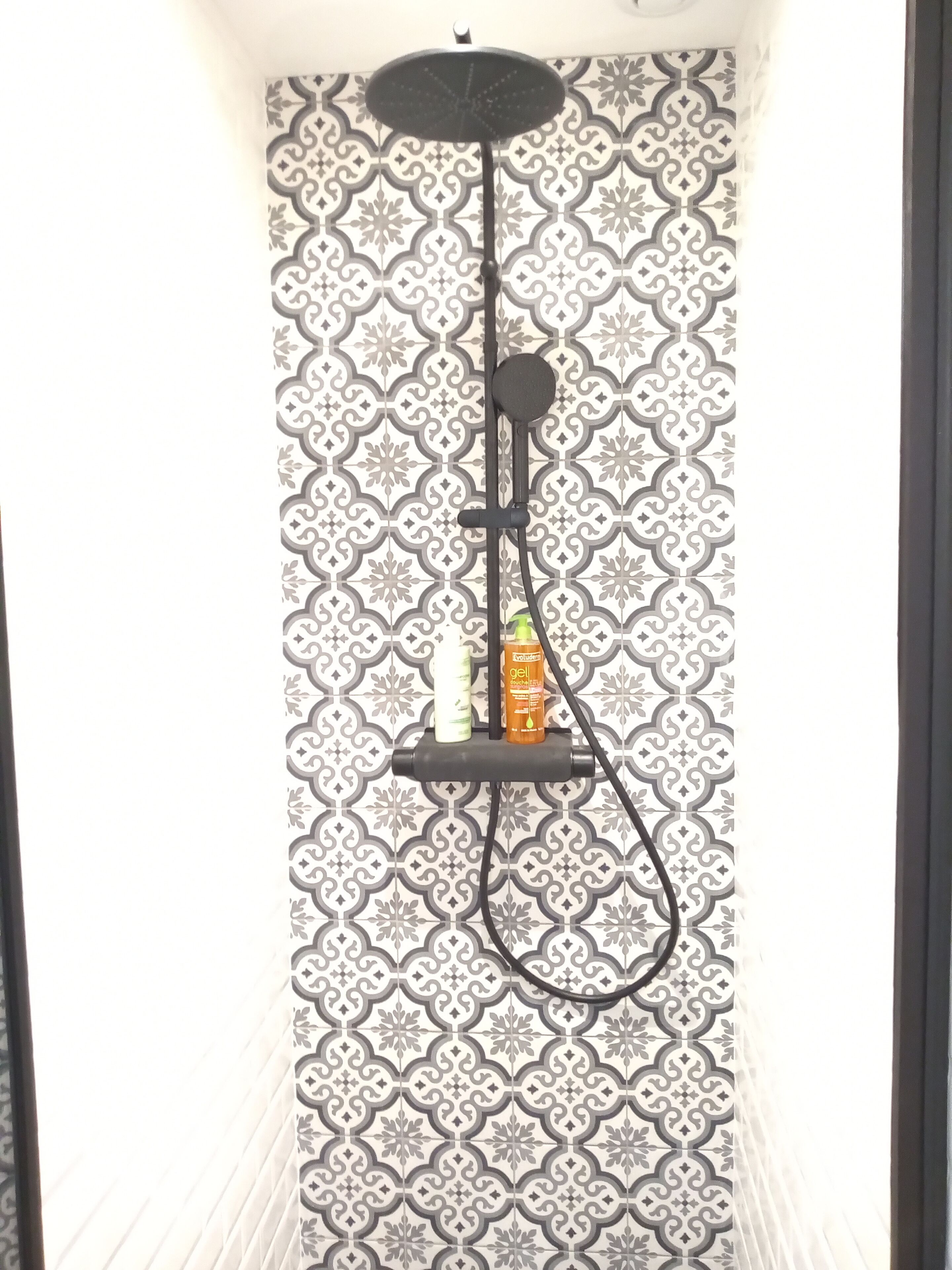 A shower with a black handheld showerhead and a wall-mounted control panel.