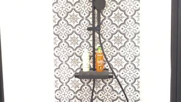 A shower with a black handheld showerhead and a wall-mounted control panel.