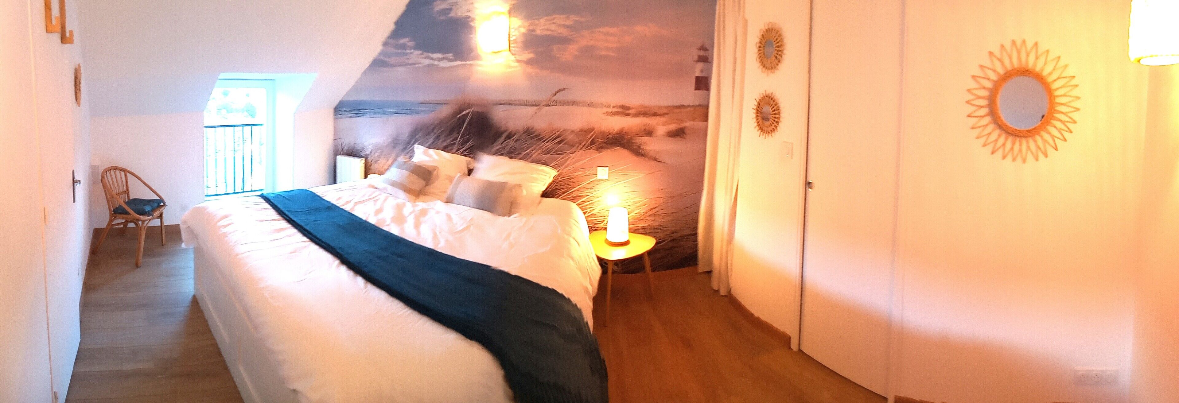 Ein Schlafzimmer mit einem Bett, einem Nachttisch, einem Sessel und einer Wandmalerei mit einer Strandansicht.