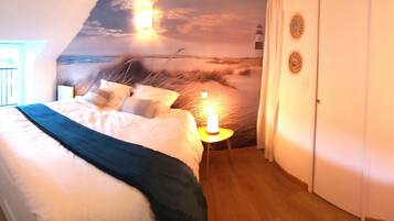 Ein Schlafzimmer mit einem Bett, einem Nachttisch, einem Sessel und einer Wandmalerei mit einer Strandansicht.