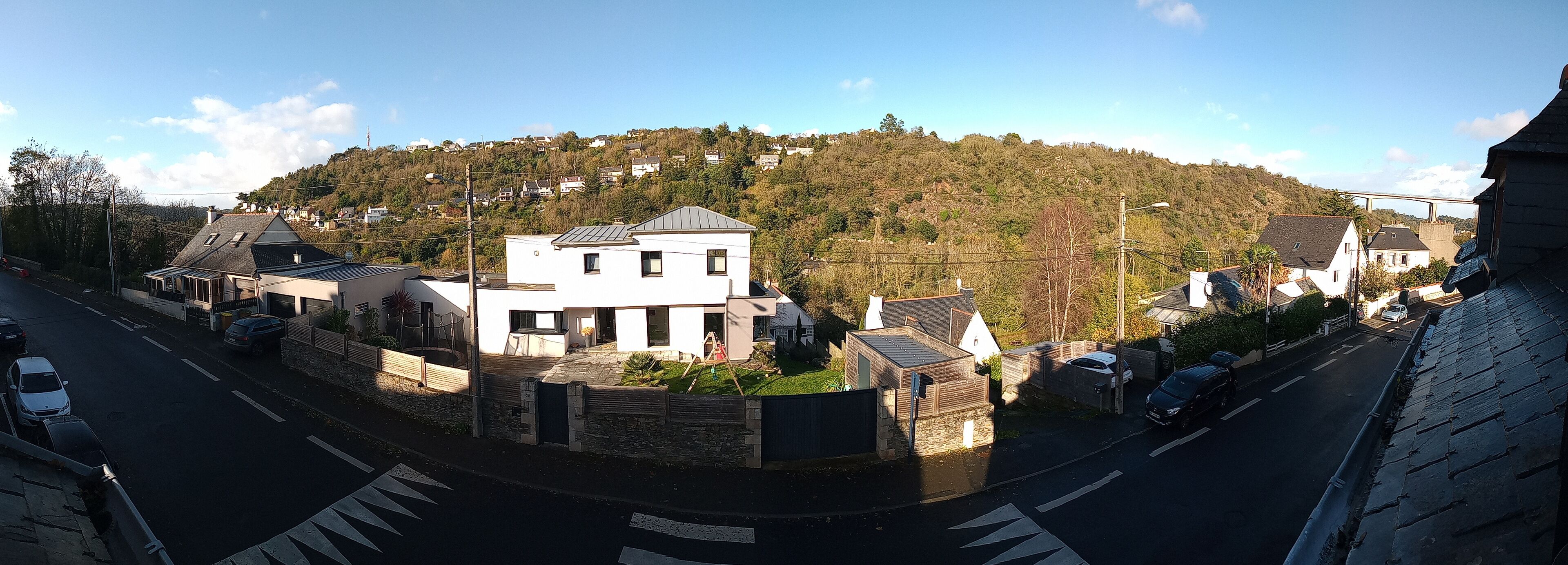 Une rue résidentielle bordée de maisons, un ciel dégag é et une colline en arrière-plan.