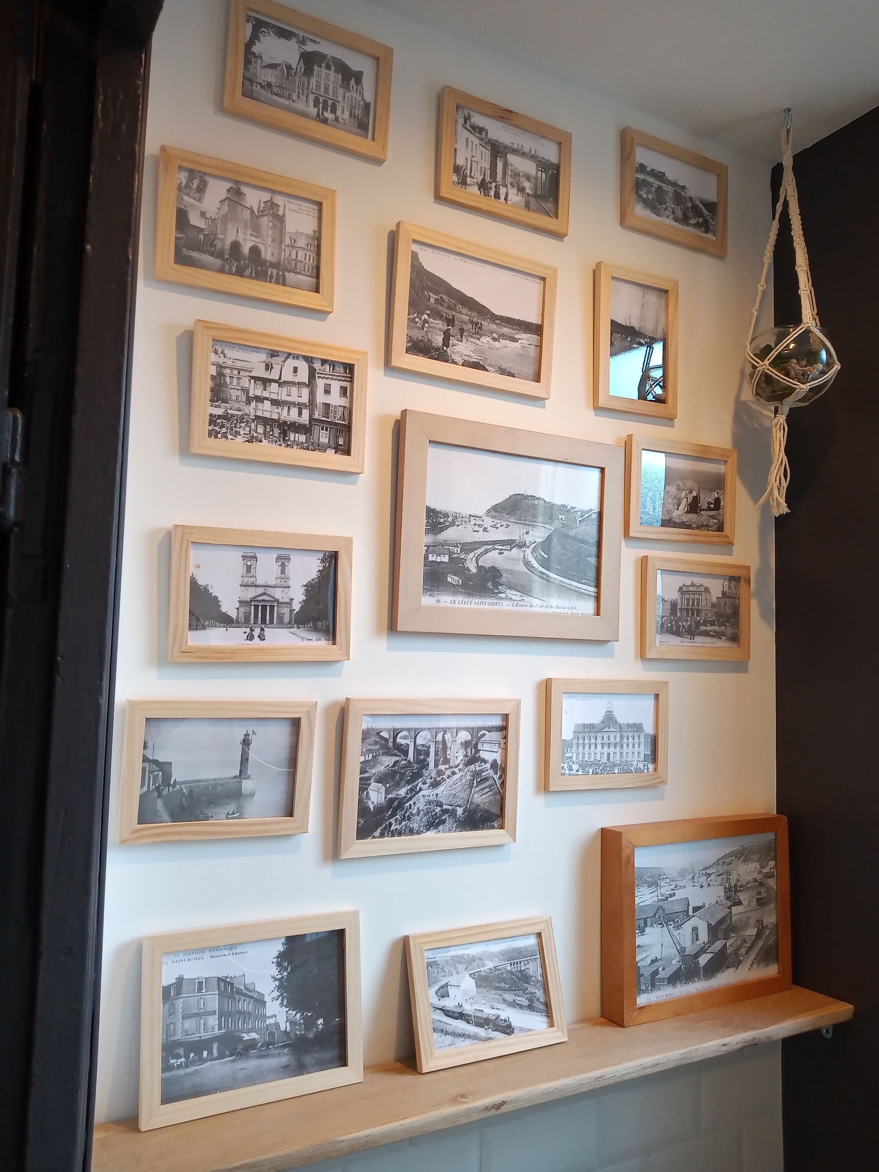 A wall with multiple black and white photographs in wooden frames, some with text captions, and a macrame hanging light fixture.