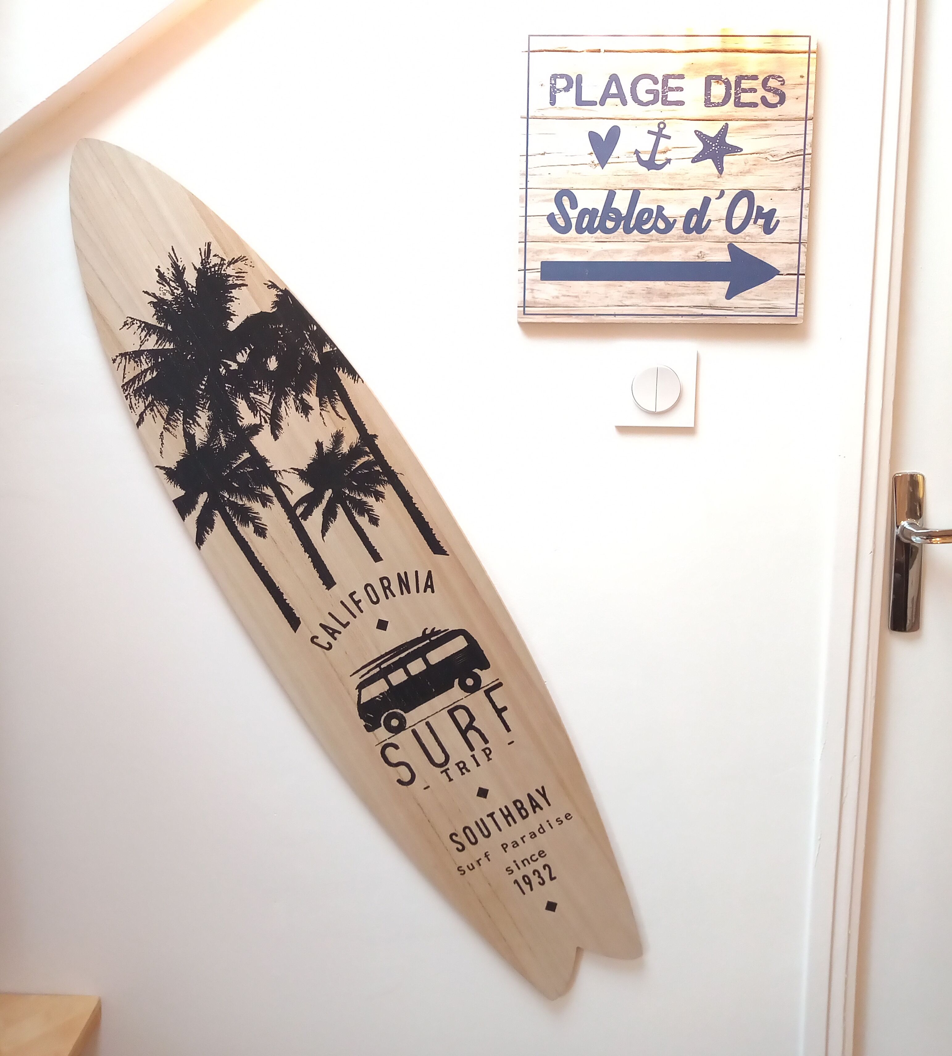 A surfboard with text and palm trees, a door, and a sign with text and an arrow.