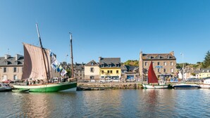 En havn med flere både, en bygning i sten med gul facade, og en klar blå himmel.