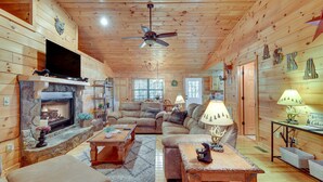 A cozy log cabin interior with a fireplace, comfortable seating, and a television.