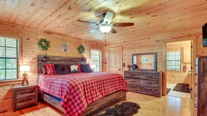 A wooden cabin bedroom with a bed, dresser, and a ceiling fan.