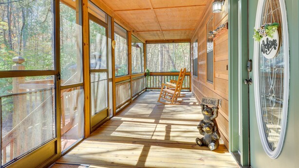 A wooden porch with a bench, a welcome sign, and a bear statue.