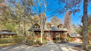A two-story log cabin with a porch, surrounded by a forested area.