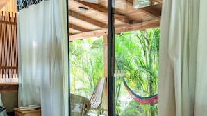 A wooden-floored room with a sliding glass door leading to a deck with a hammock and lush greenery. - Playa Pelada Beachfront Bungalow at villas Ecositas Nosara (Provincia de Guanacaste)