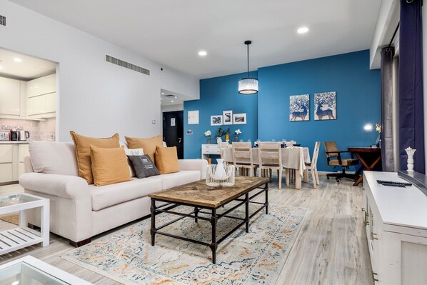 A modern living room with a white sofa, a coffee table, and a dining area with a white table and chairs.