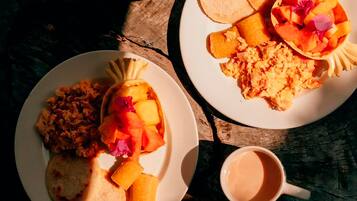 Dos platos de comida con fruta y huevos revueltos, una taza de café y una mesa de madera rústica.