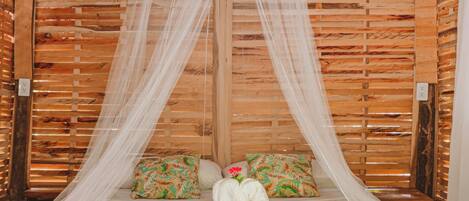A bed with a white canopy and pillows, set against a wooden wall with a woven ceiling.